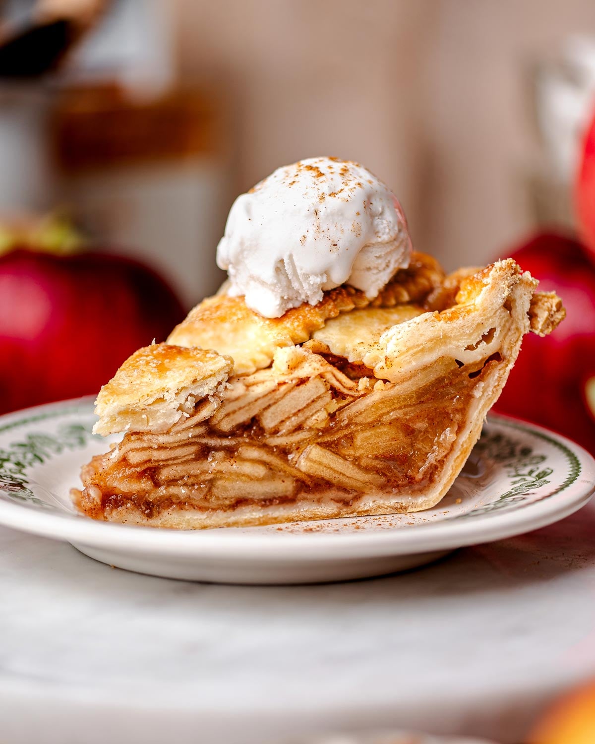 A slice of vegan apple pie with a golden flaky crust, stacked neatly with tender apple slices and topped with a scoop of vanilla non-dairy ice cream.