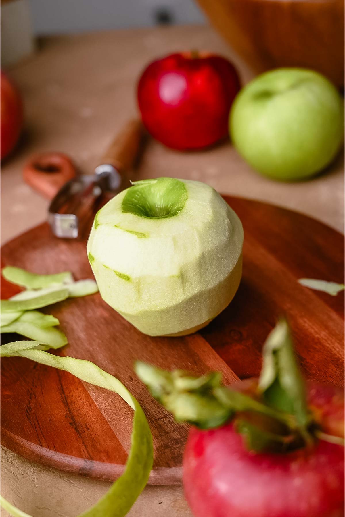 A peeled Grannysmith apple on a dark wood board.