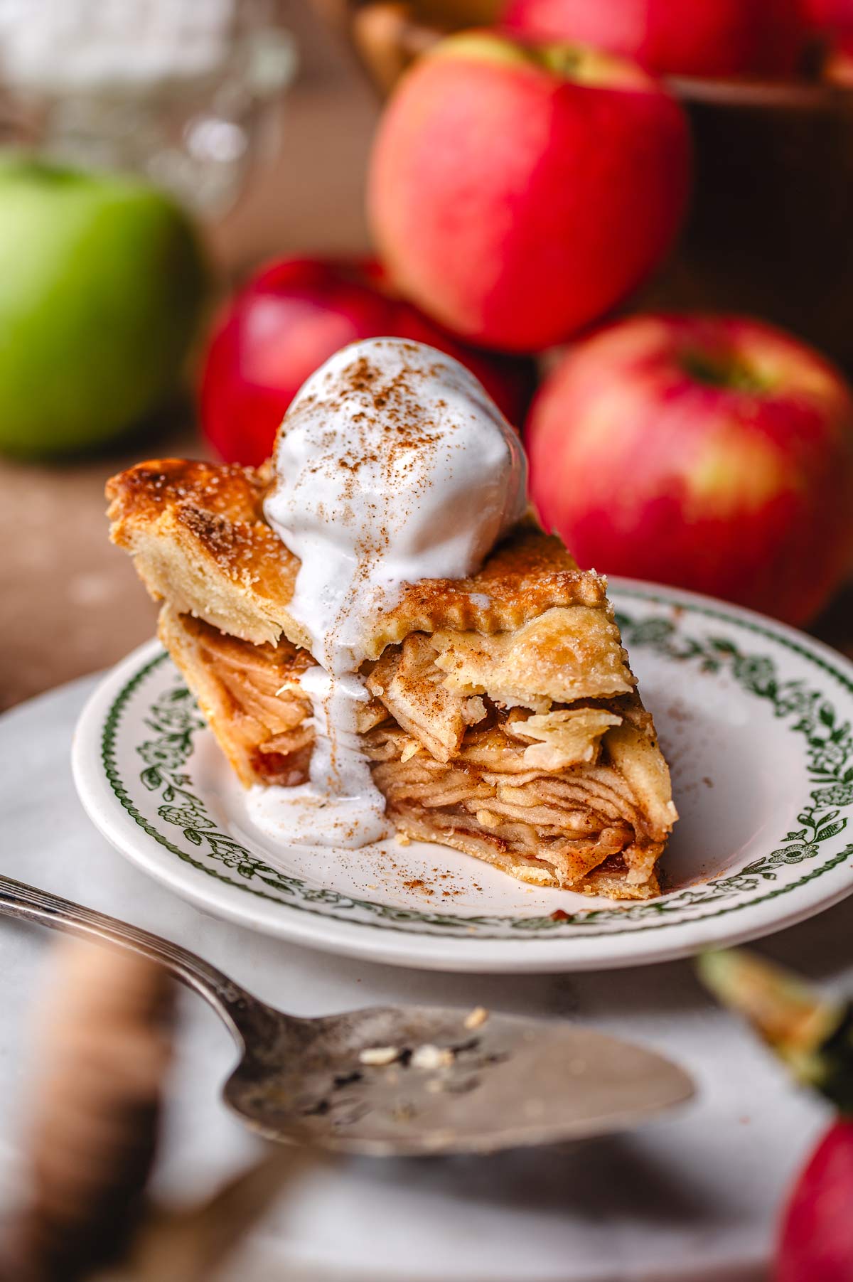 a slice of vegan apple pie with a scoop of coconut whipped cream melting on top.