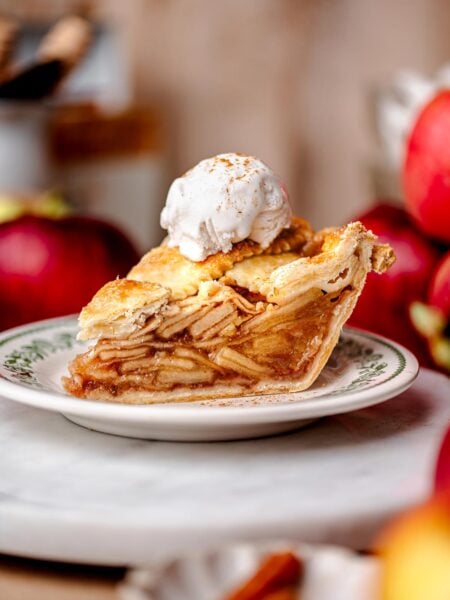 A slice of vegan apple pie with a golden flaky crust, stacked neatly with tender apple slices and topped with a scoop of vanilla non-dairy ice cream.