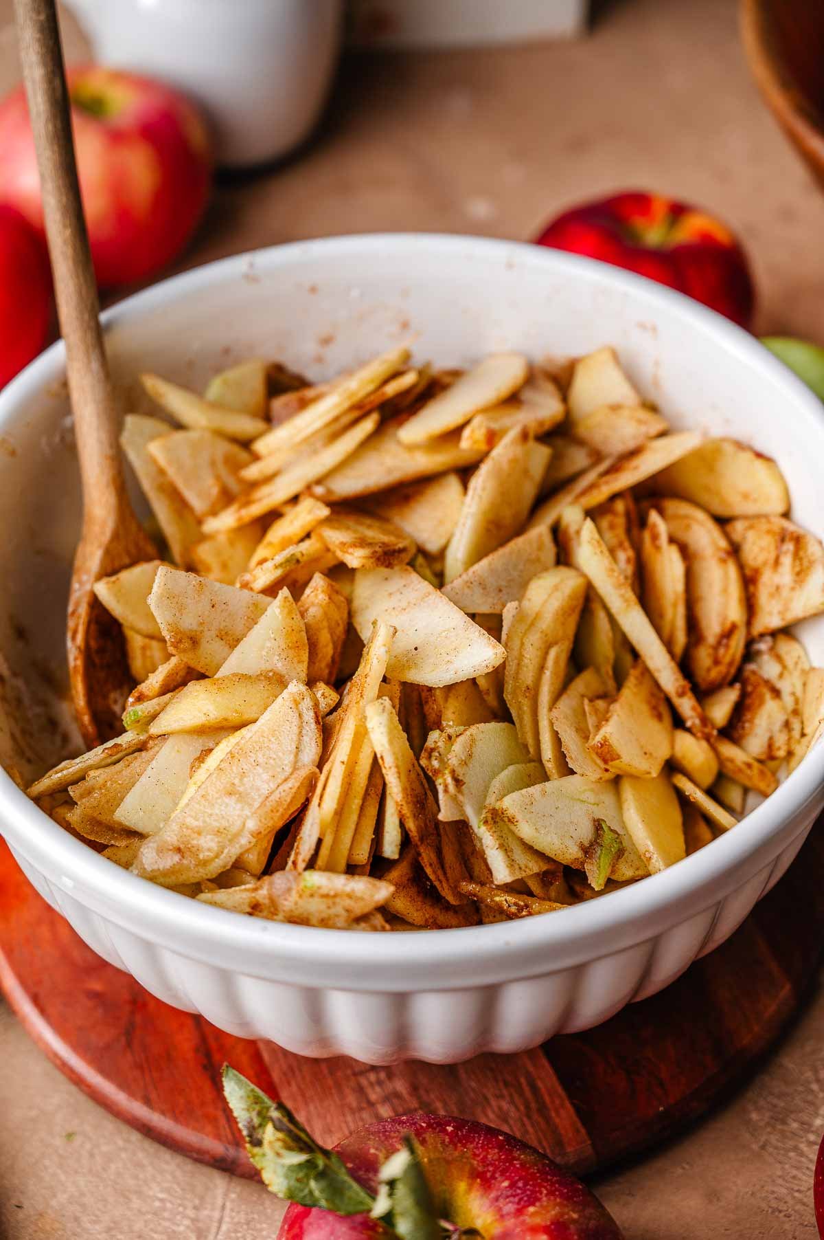 Overhead view of a mixing bowl with evenly coated spiced apple slices stirred together with sugar, spice, and thickener for vegan apple pie.