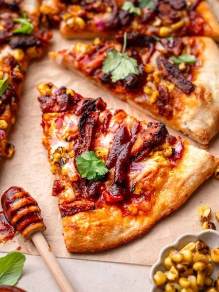 a slice of vegan bbq chicken pizza on parchment paper with fresh cilantro and charred corn.