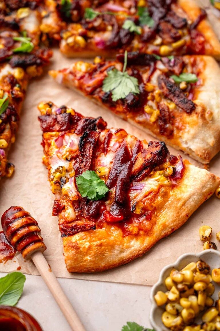 a slice of vegan bbq chicken pizza on parchment paper with fresh cilantro and charred corn.