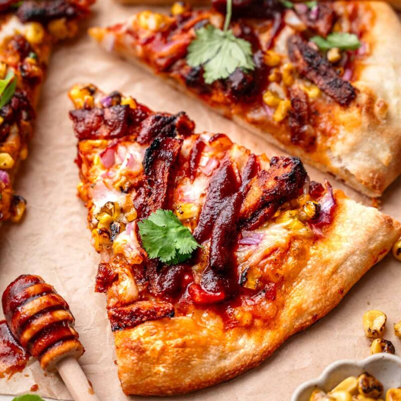 a slice of vegan bbq chicken pizza on parchment paper with fresh cilantro and charred corn.