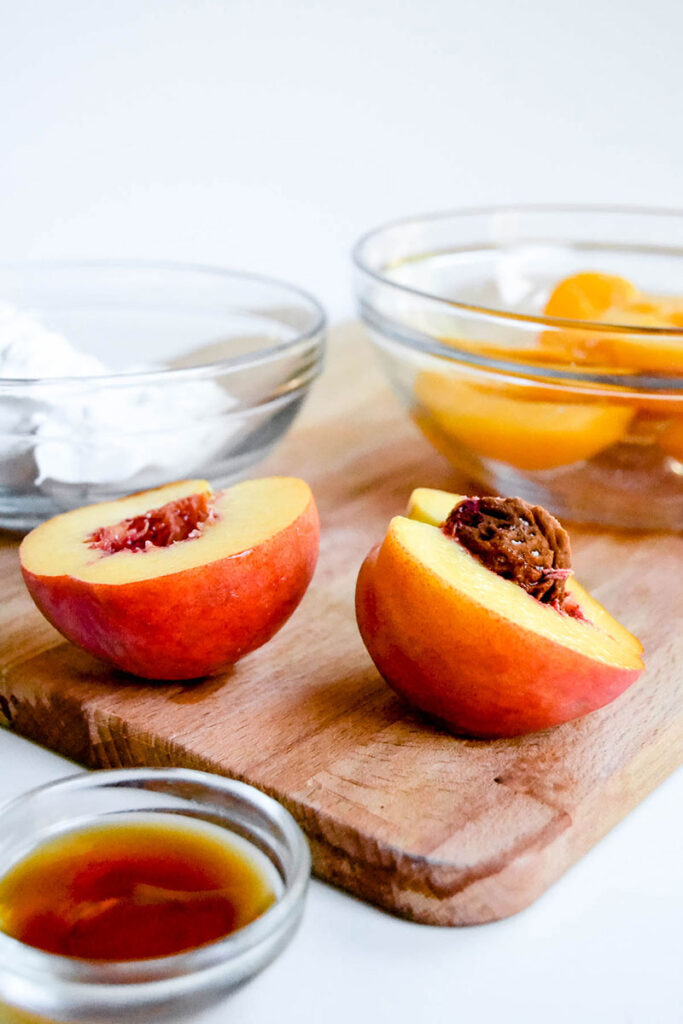 a ripe peach cut in half on a wooden cutting board.