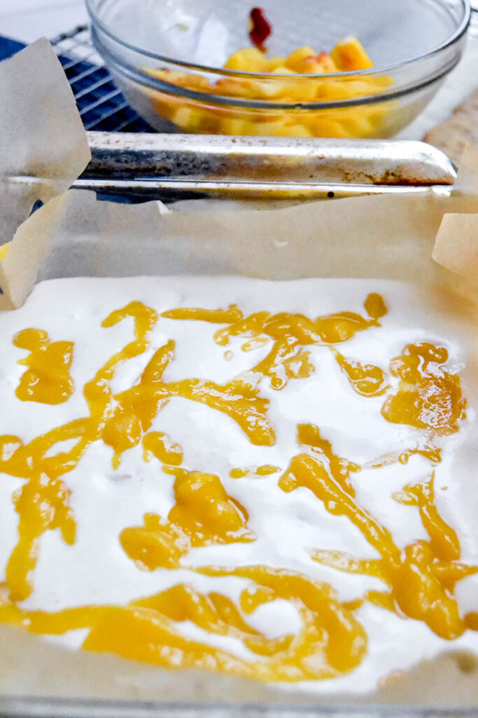 swirled peach puree in the coconut milk ice cream in a glass square baking dish.