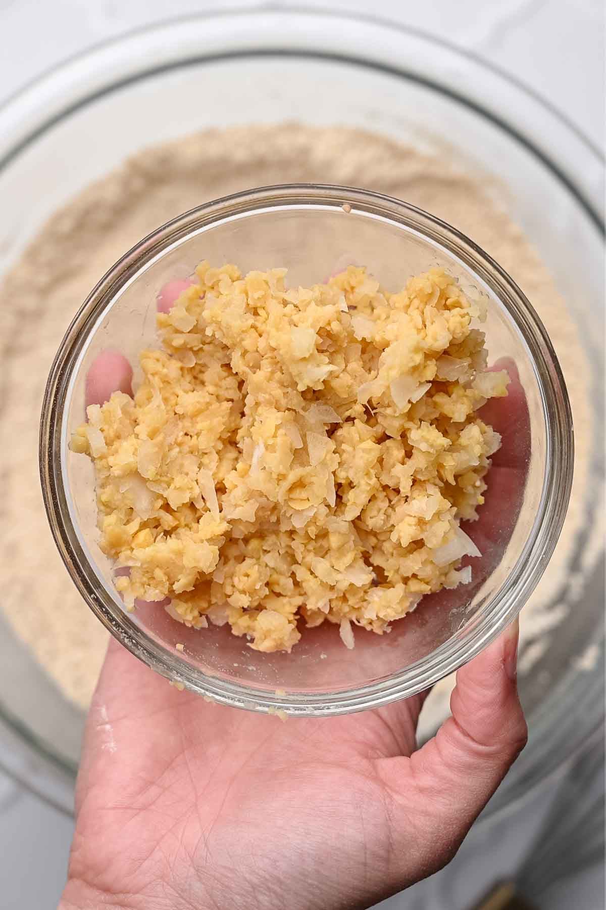 finely minced chickpeas and onion in a medium bowl being held by a hand.