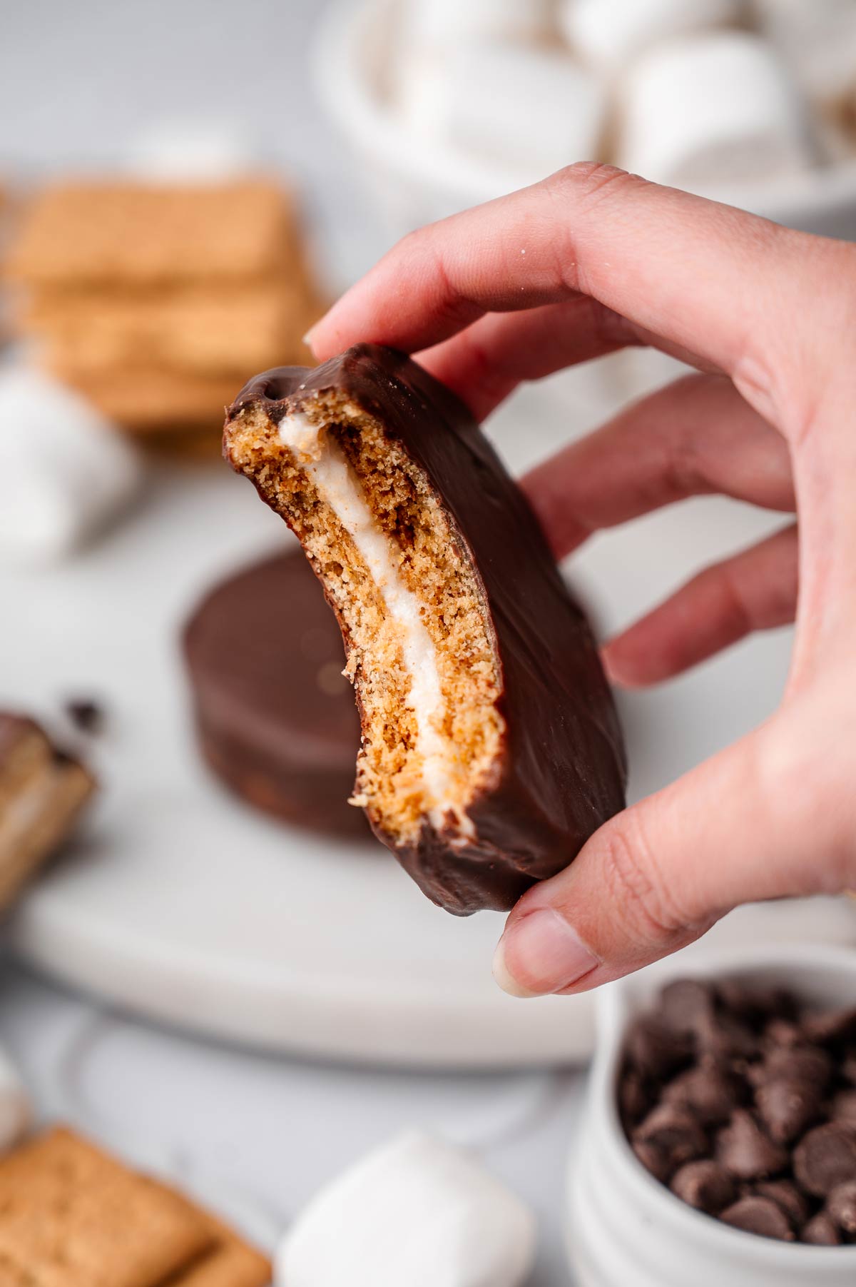 a hand holding a half eaten moon pie exposing the marshmallow center.