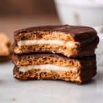 two homemade vegan moon pies stacked on each other with a bite taken out of them exposing the marshmallow center.