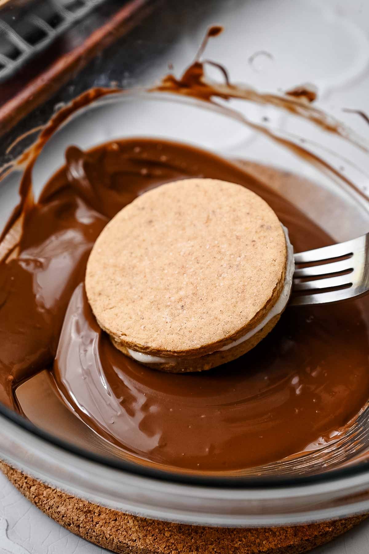 an uncoated moon pie being dipped into melted chocolate with a fork.