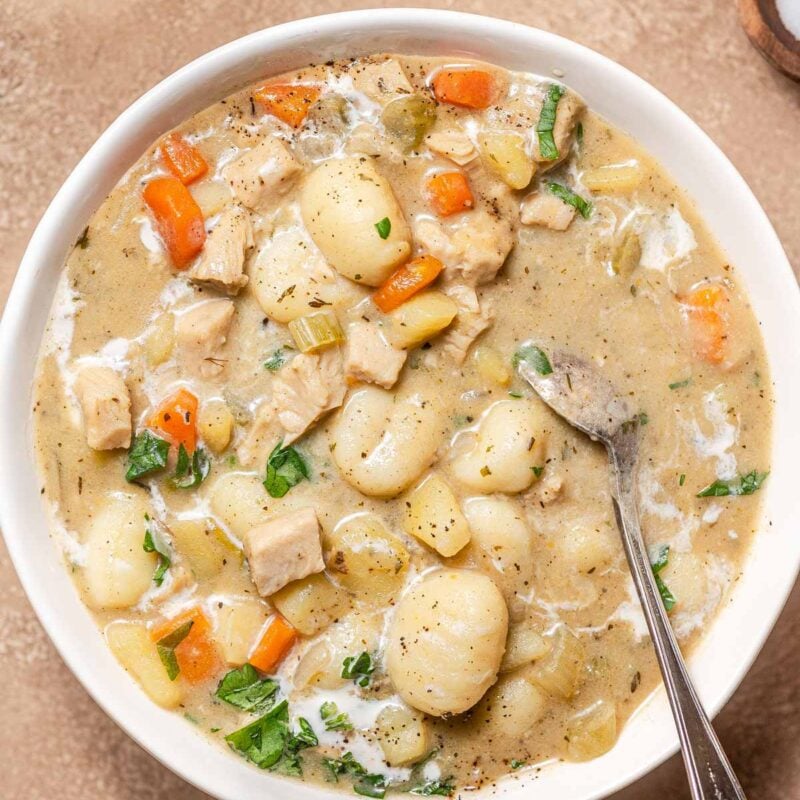 creamy vegan gnocchi soup in a white bowl with herbs.