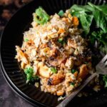 a black plate with vegan rice casserole with mushrooms and silver fork.