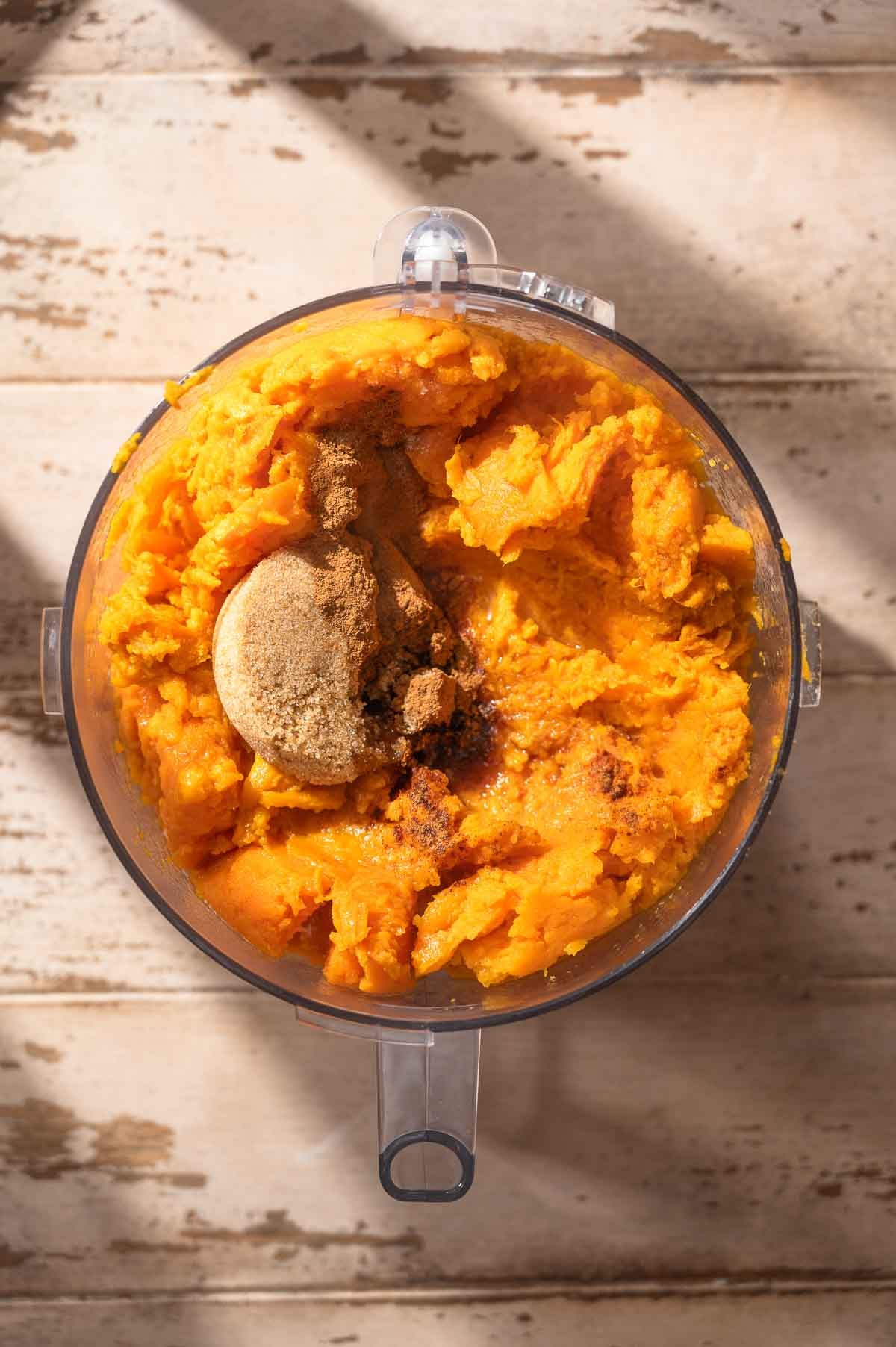 a food processor bowl with baked sweet potatoes, brown sugar and melted vegan butter.