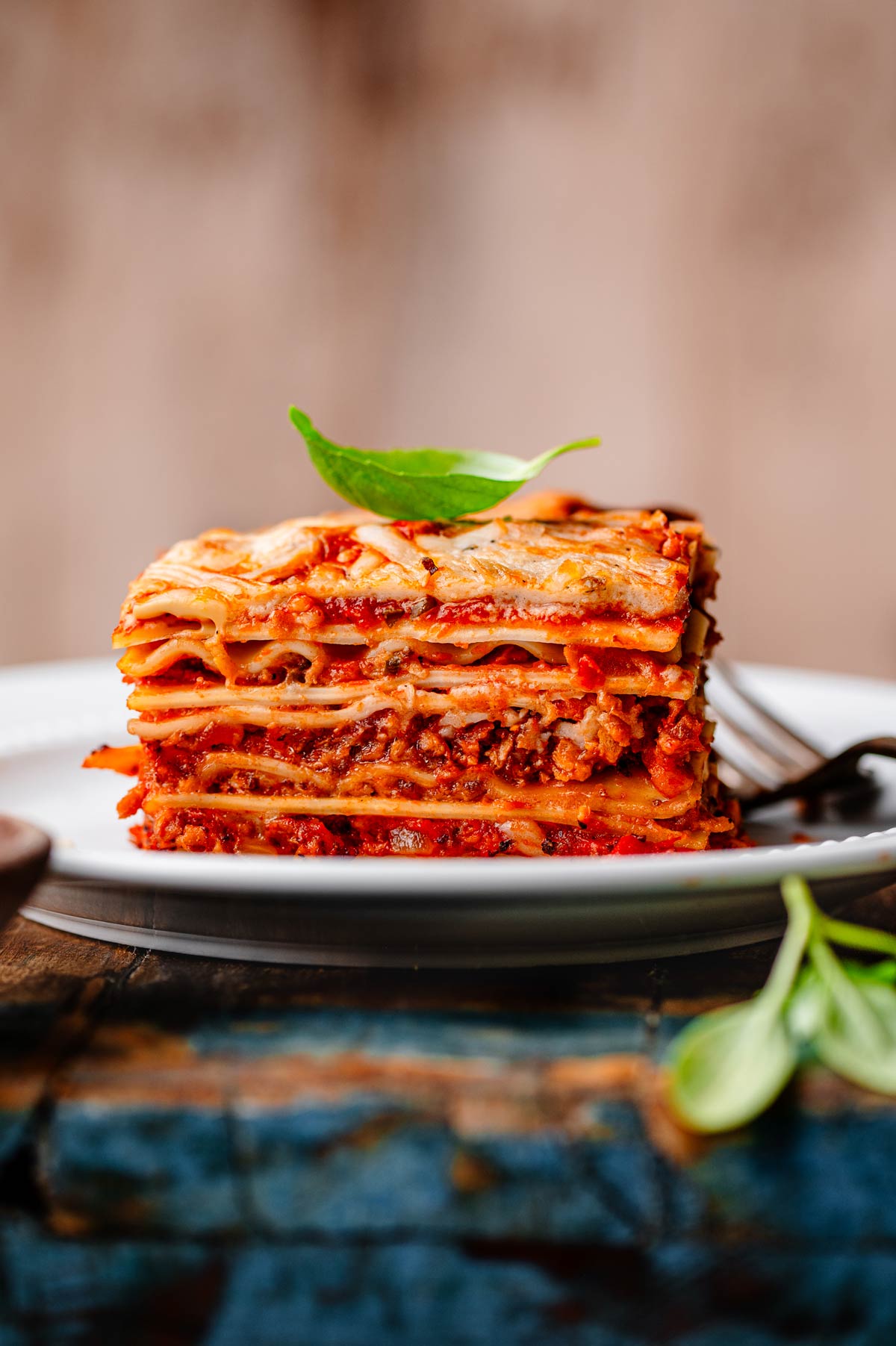 Close-up of a slice of vegan lasagna with creamy béchamel, plant-based ground beef, and golden melted top, garnished with fresh basil.