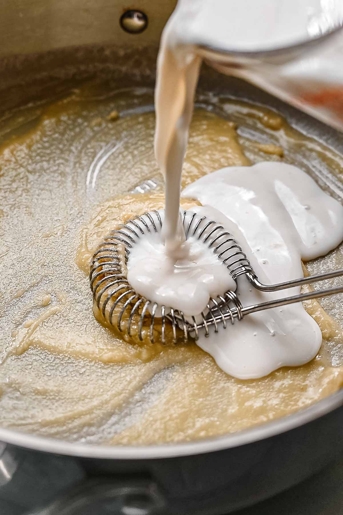 dairy free milk being poured into a roux.