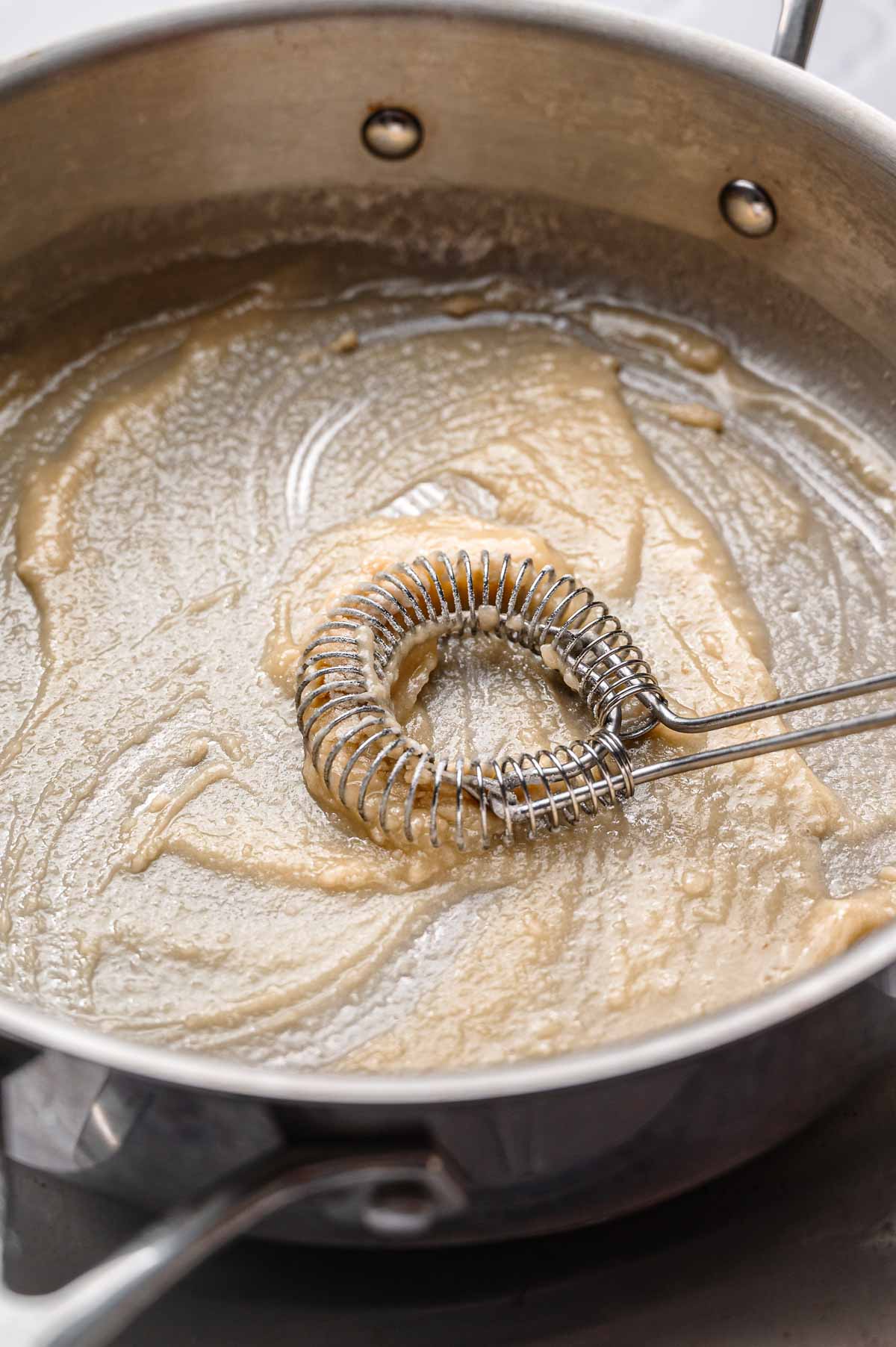 a metal whisk mixing flour into melted vegan butter.