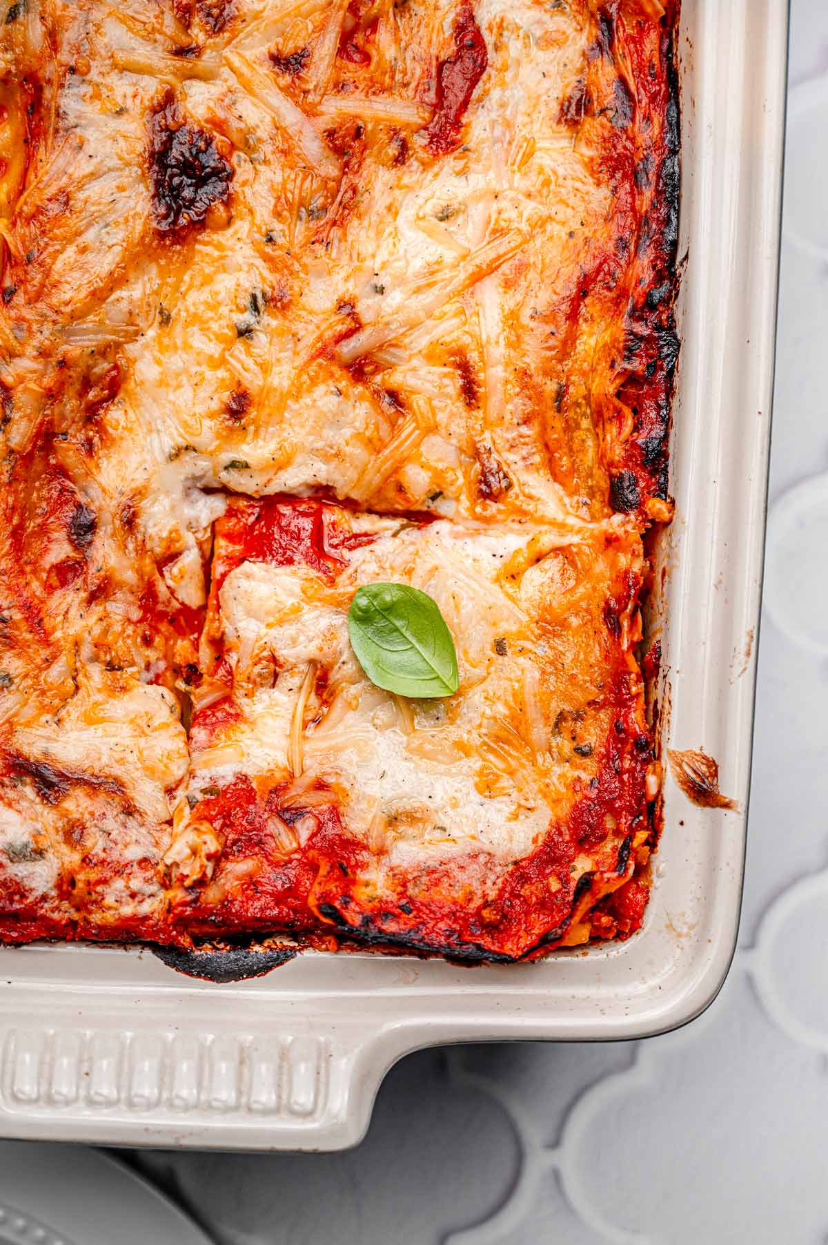 Overhead view of baked vegan béchamel lasagna with one corner slice removed, showing creamy layers and browned edges.