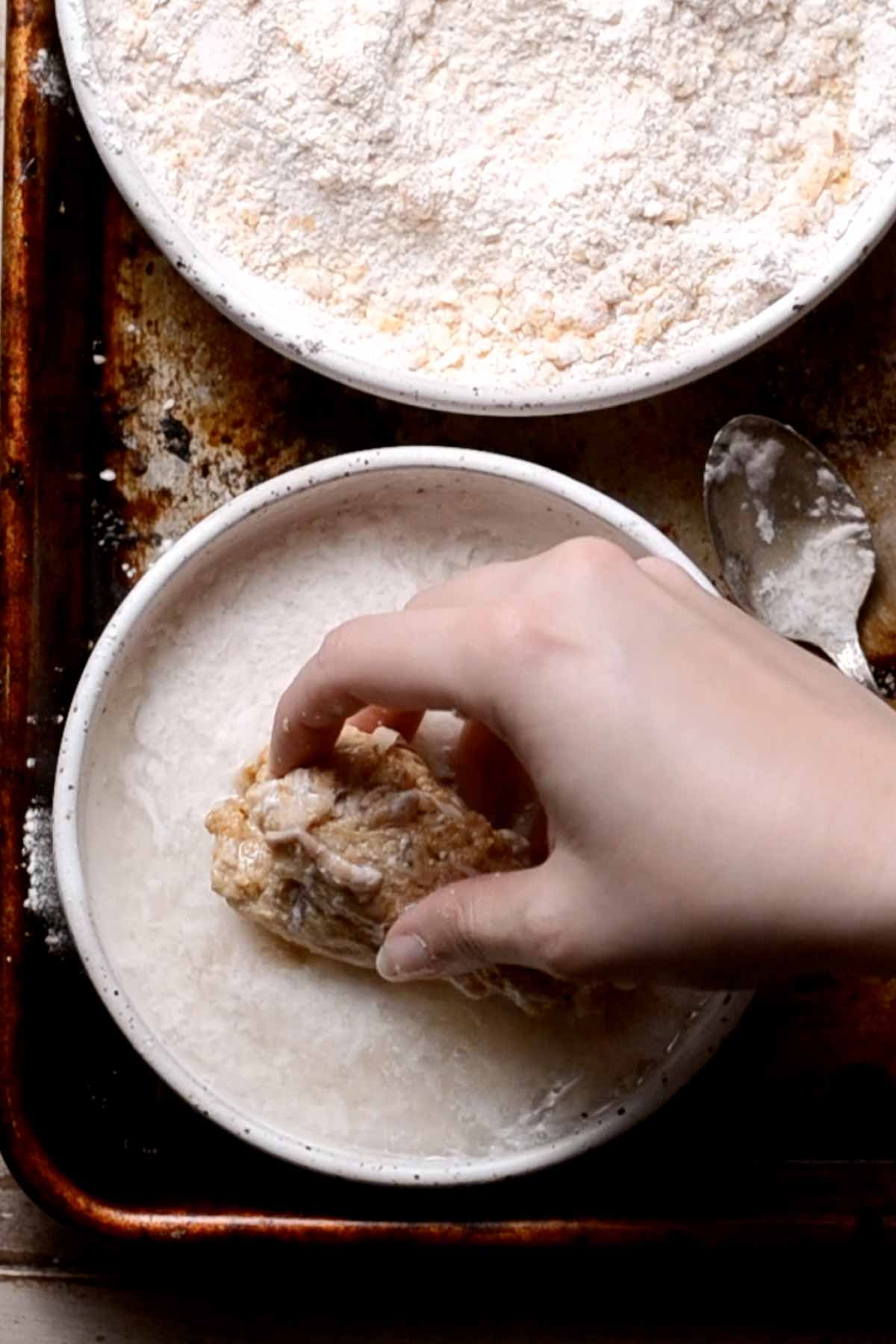 a hand dunking vegan chicken in buttermilk.