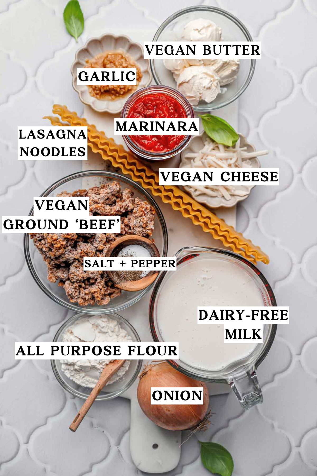 Flat lay of ingredients for vegan lasagna including vegan ground beef, marinara, dairy-free milk, vegan cheese, onion, garlic, and lasagna noodles.