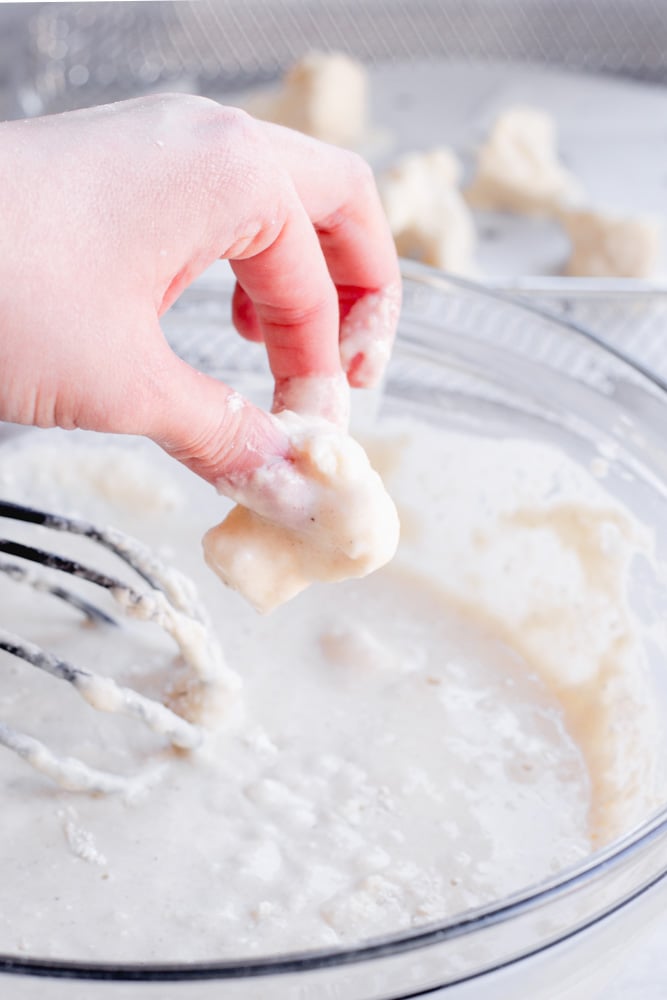 a hand dipping a cauliflower floret into the tempura batter.