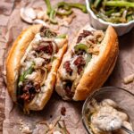 two vegan philly cheesesteaks filled with seitan, peppers and onions on parchment paper.