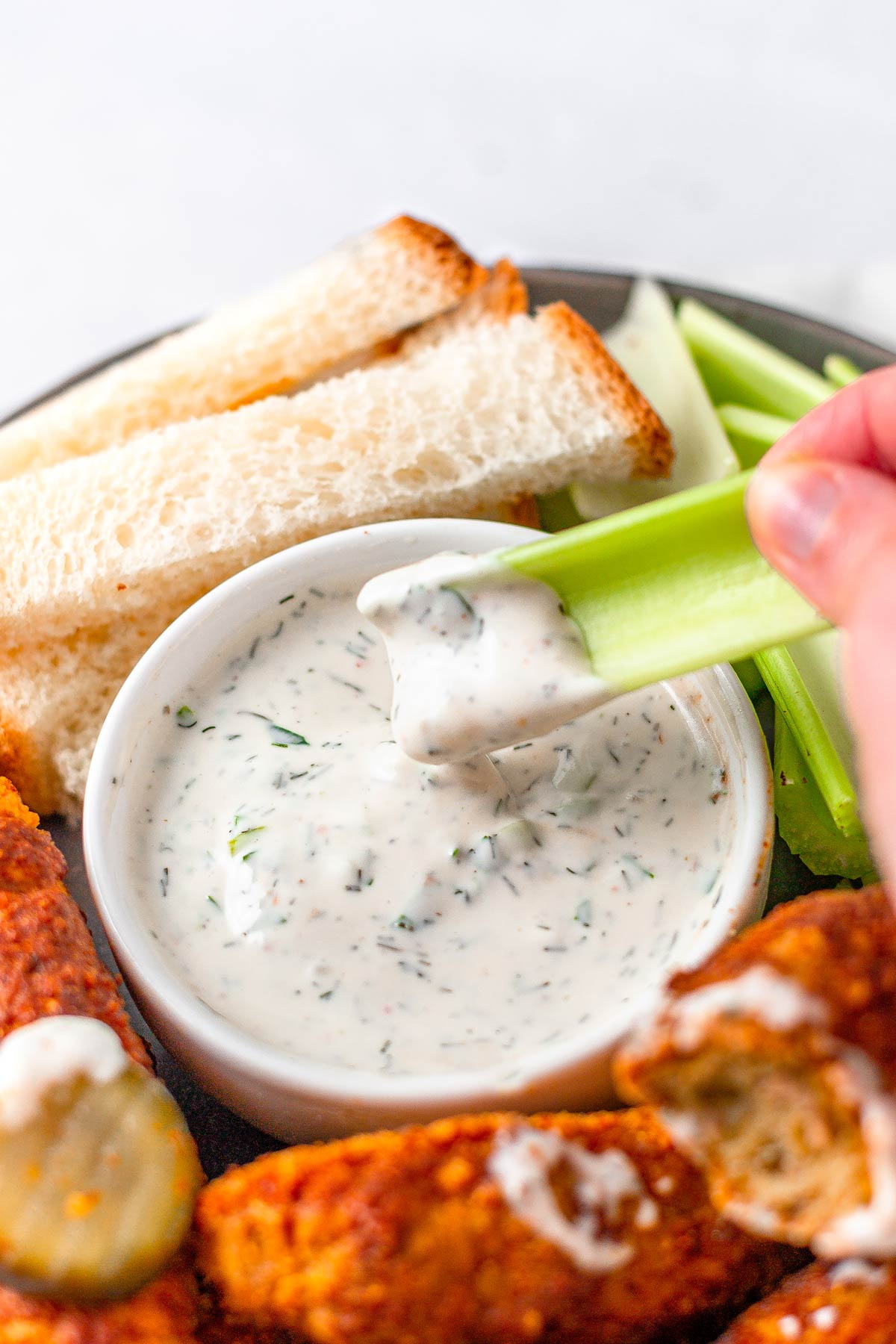 a hand dipping a celery stick in a bowl of homemade vegan ranch dressing.