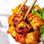 crispy orange tofu being gripped by chopsticks.