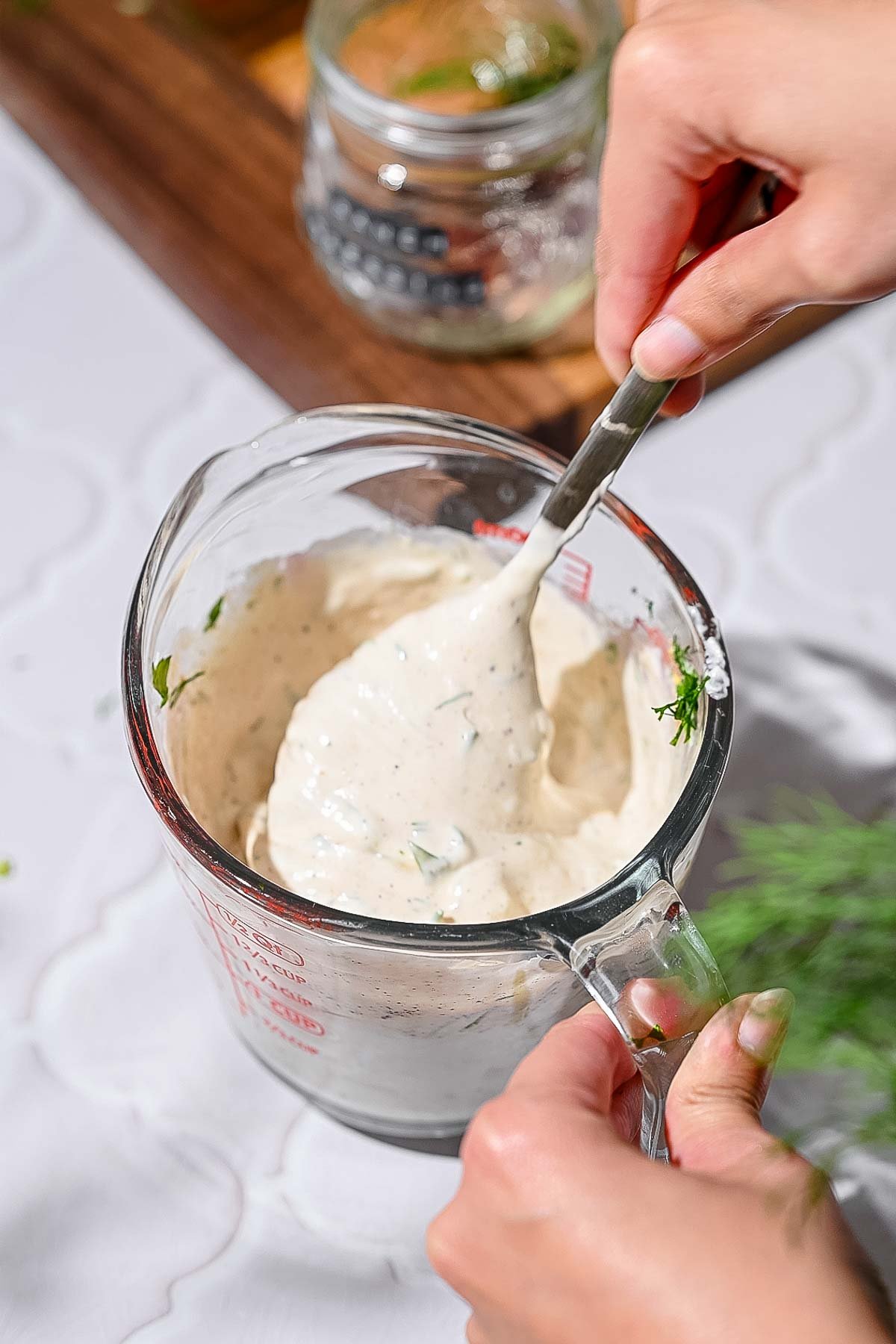 a hand using a spoon to mix the ranch ingredients in a measuring cup.