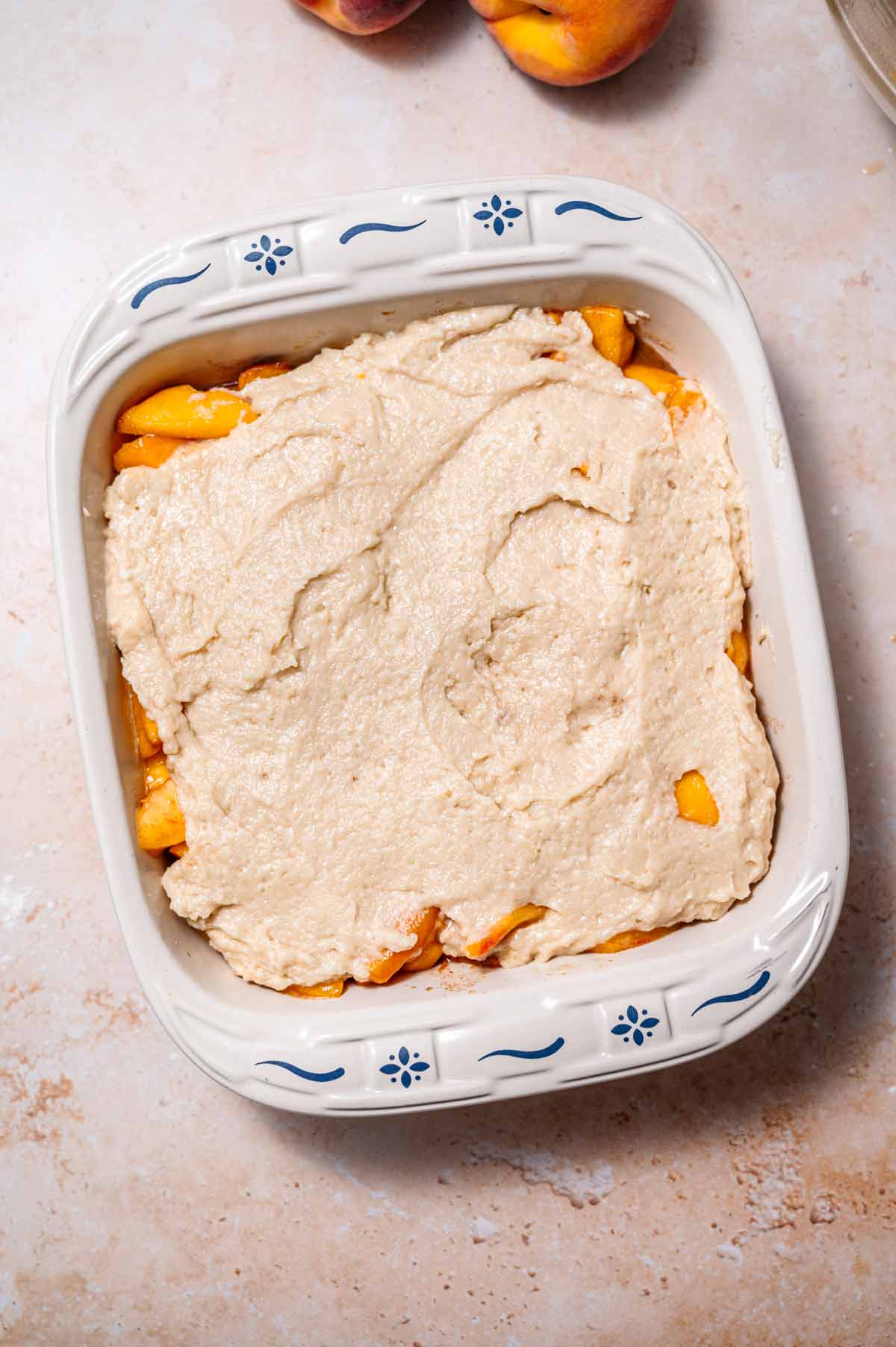 the unbaked peach cobbler on a tan stone surface.
