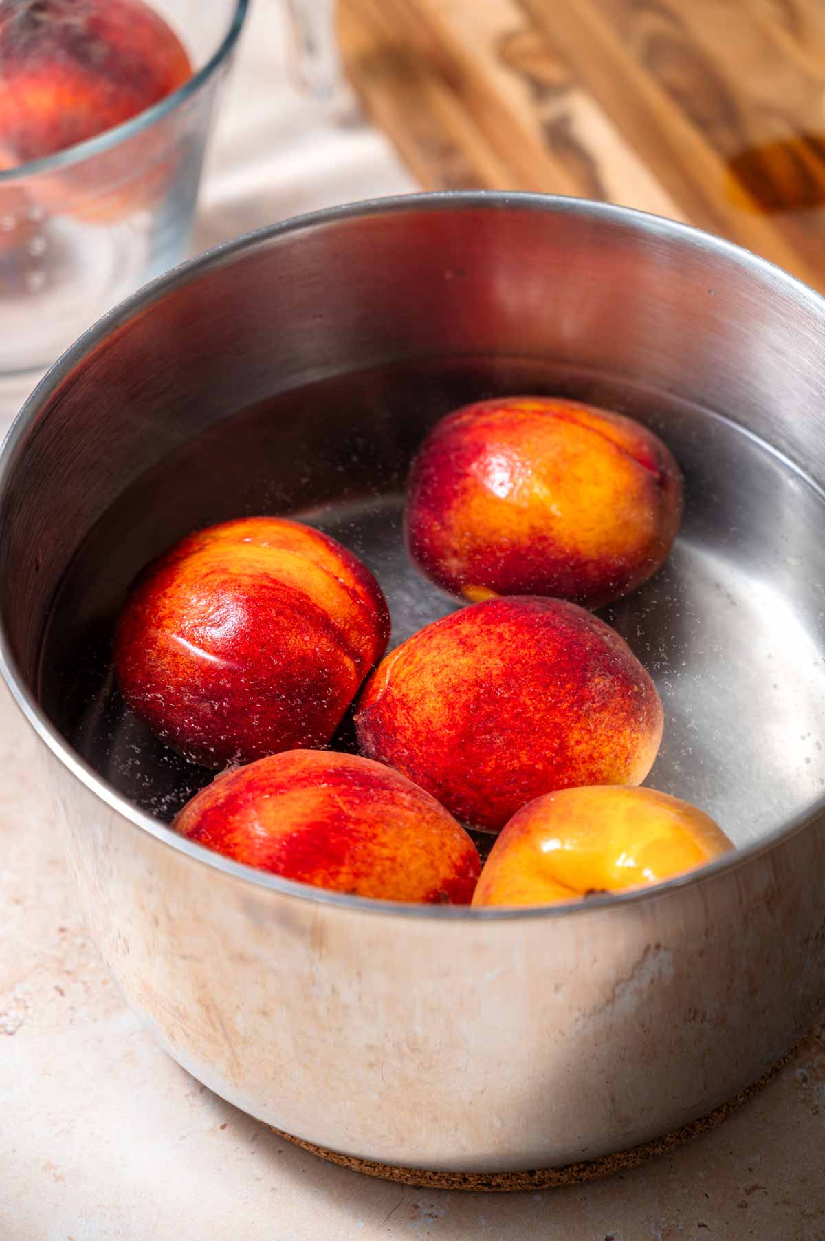 a silver pot filled with hot water and five whole peaches.