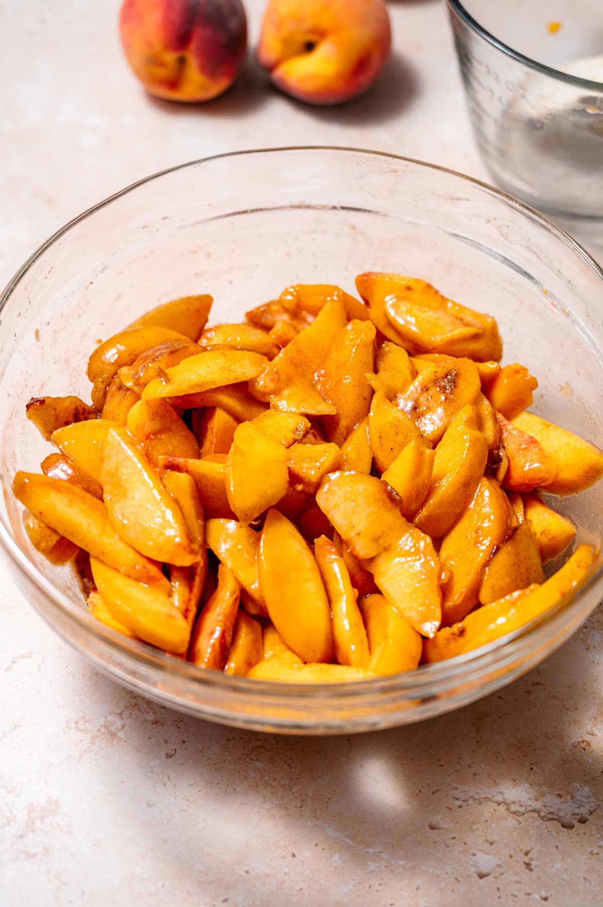 a large glass bowl with sliced peaches and cobbler filling.