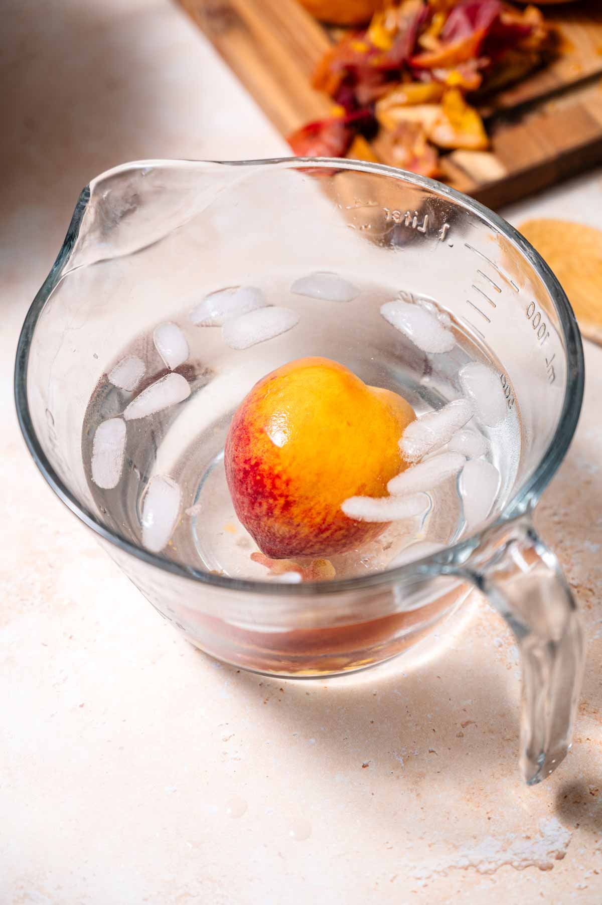 a single whole peach in a large measuring cup filled with ice water.