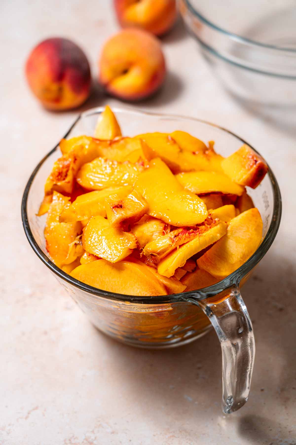 a large glass measuring cup with sliced and peeled peaches.