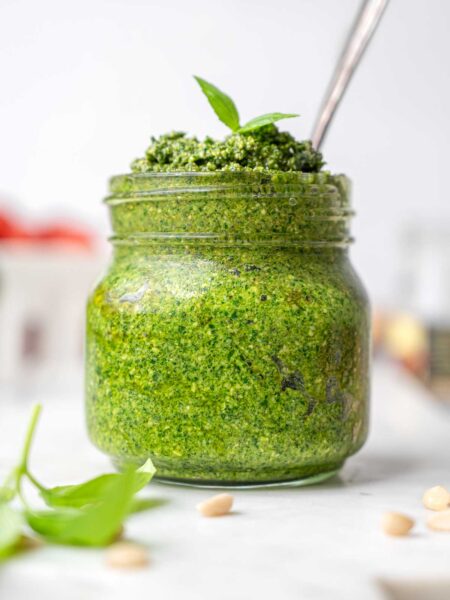 a close up of a jar filled with vegan basil pesto on a marble tray.