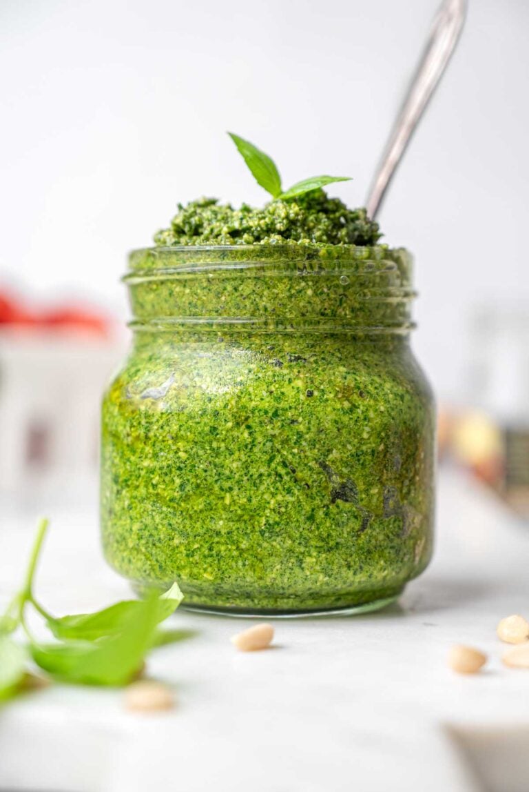 a close up of a jar filled with vegan basil pesto on a marble tray.