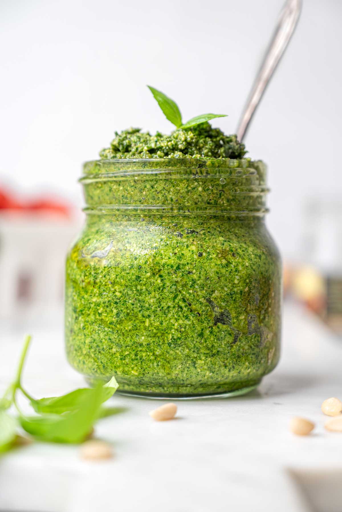 a close up of a jar filled with vegan basil pesto on a marble tray.