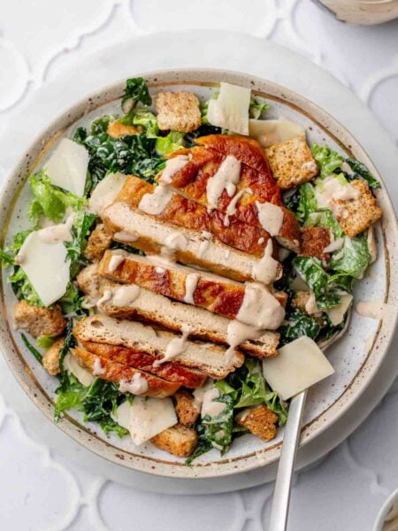 a bowl with vegan caesar salad topped with sliced baked plant-based chicken.