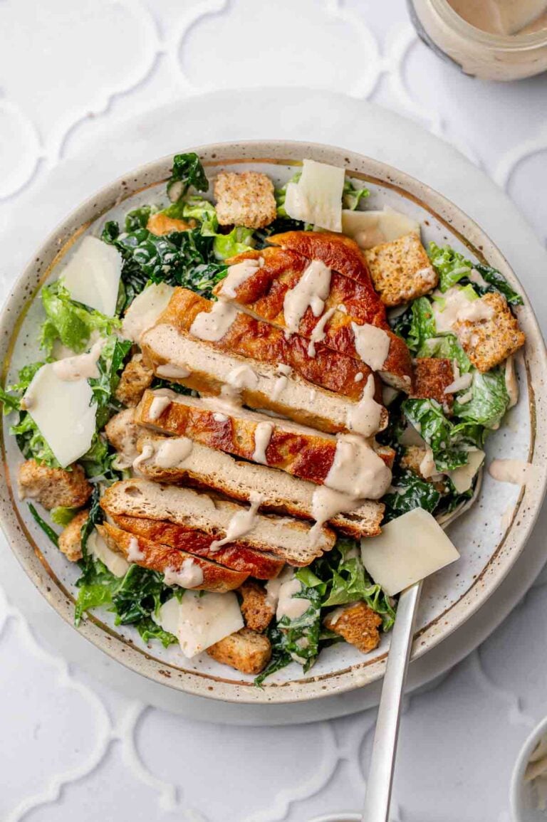 a bowl with vegan caesar salad topped with sliced baked plant-based chicken.