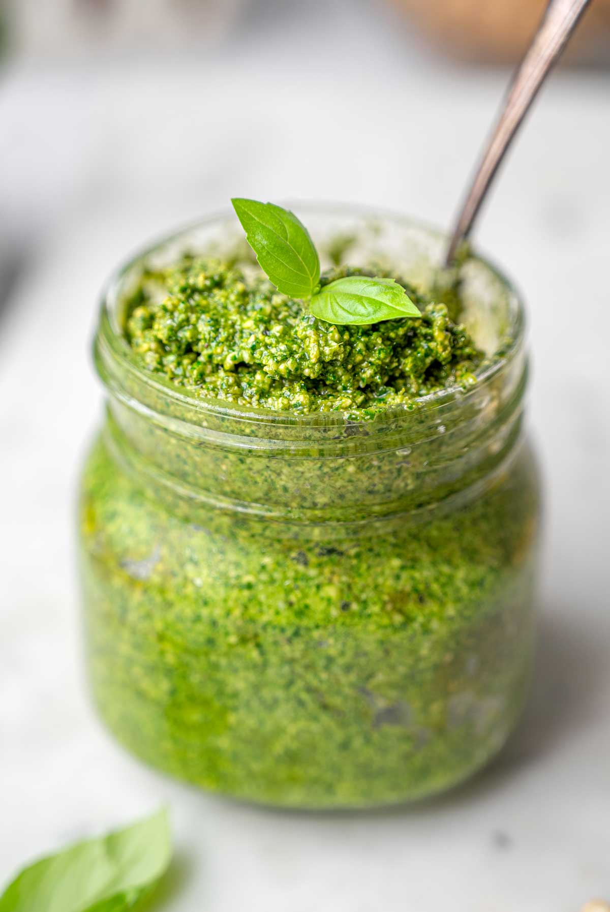 a jar of vegan pesto with small basil leaves on top.