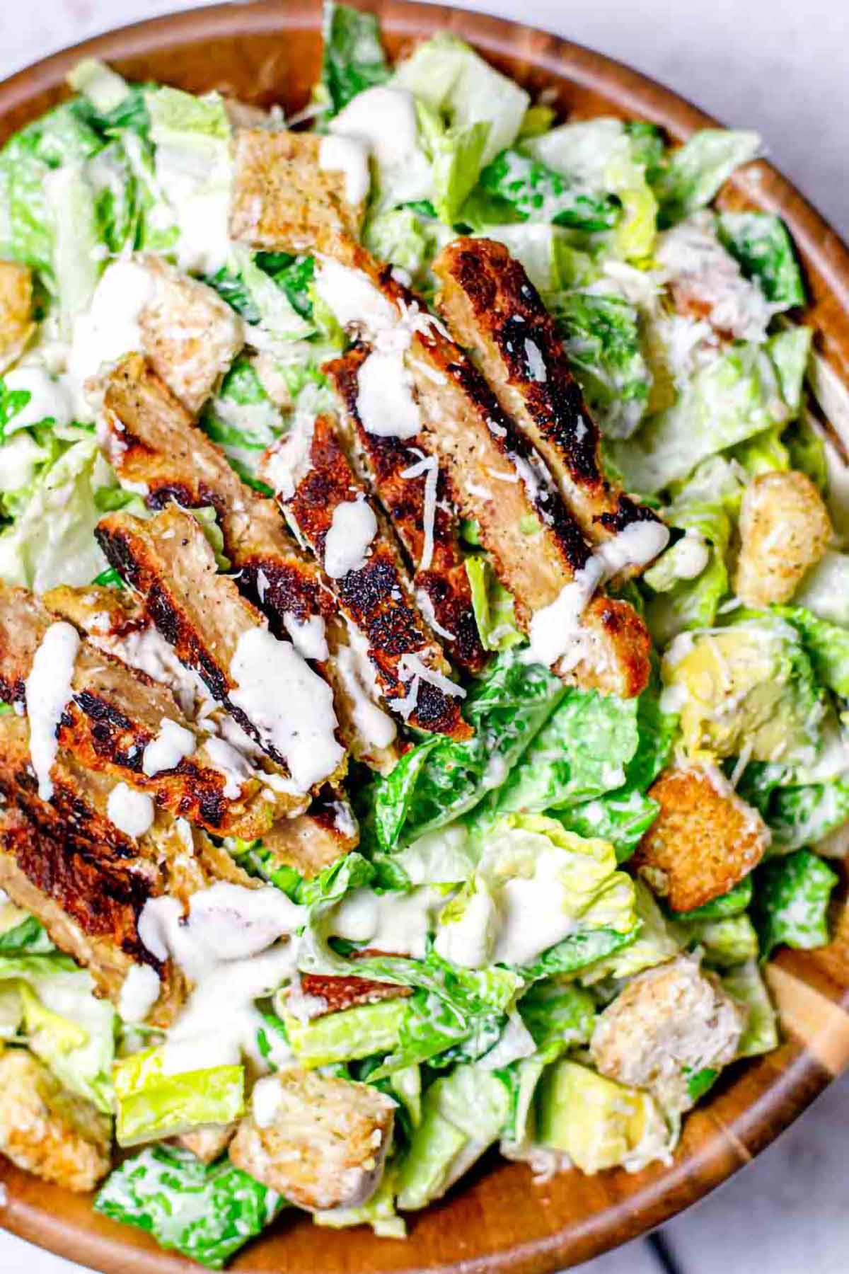 vegan caesar salad in a wooden bowl topped with baked seitan chicken.