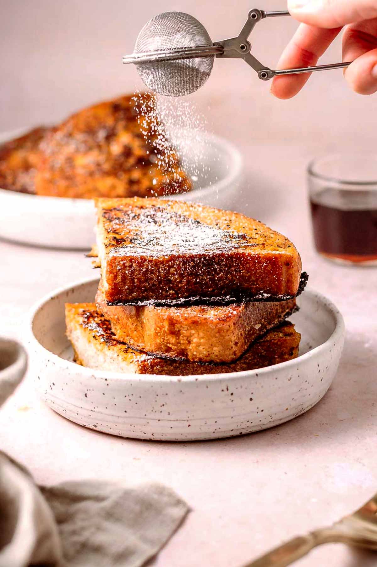 a hand adding powdered sugar to a stack of vegan french toast made with JUST egg.