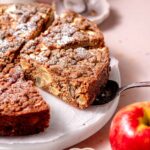 a slice of vegan apple cake on a silver spatula on a marble tray.