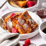 Vegan JUST Egg French Toast topped with powdered sugar, syrup and berries on a white plate.