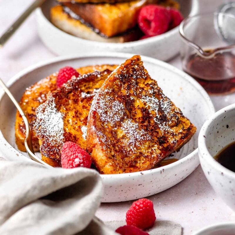 Vegan JUST Egg French Toast topped with powdered sugar, syrup and berries on a white plate.