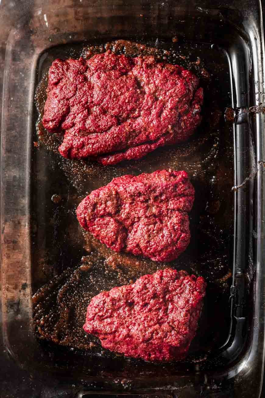 one large seitan steak and two smaller seitan steaks in an oiled pan.