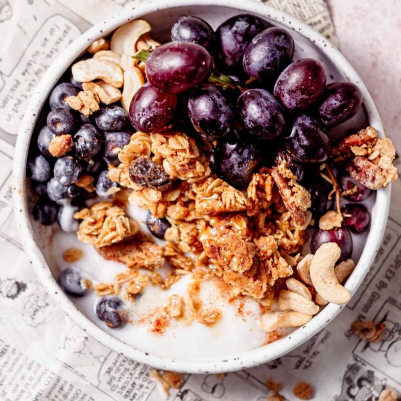 a bowl filled with dairy-free yogurt, air fryer granola and red grapes.