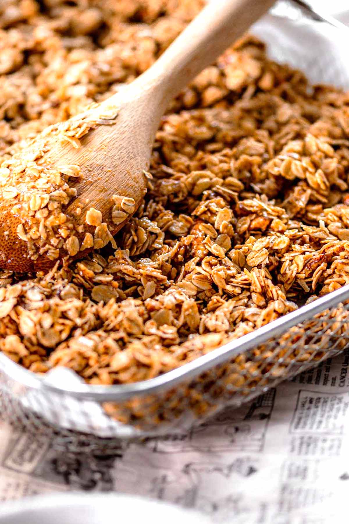 a spoon spreading the mixed granola out in the air fryer basket.