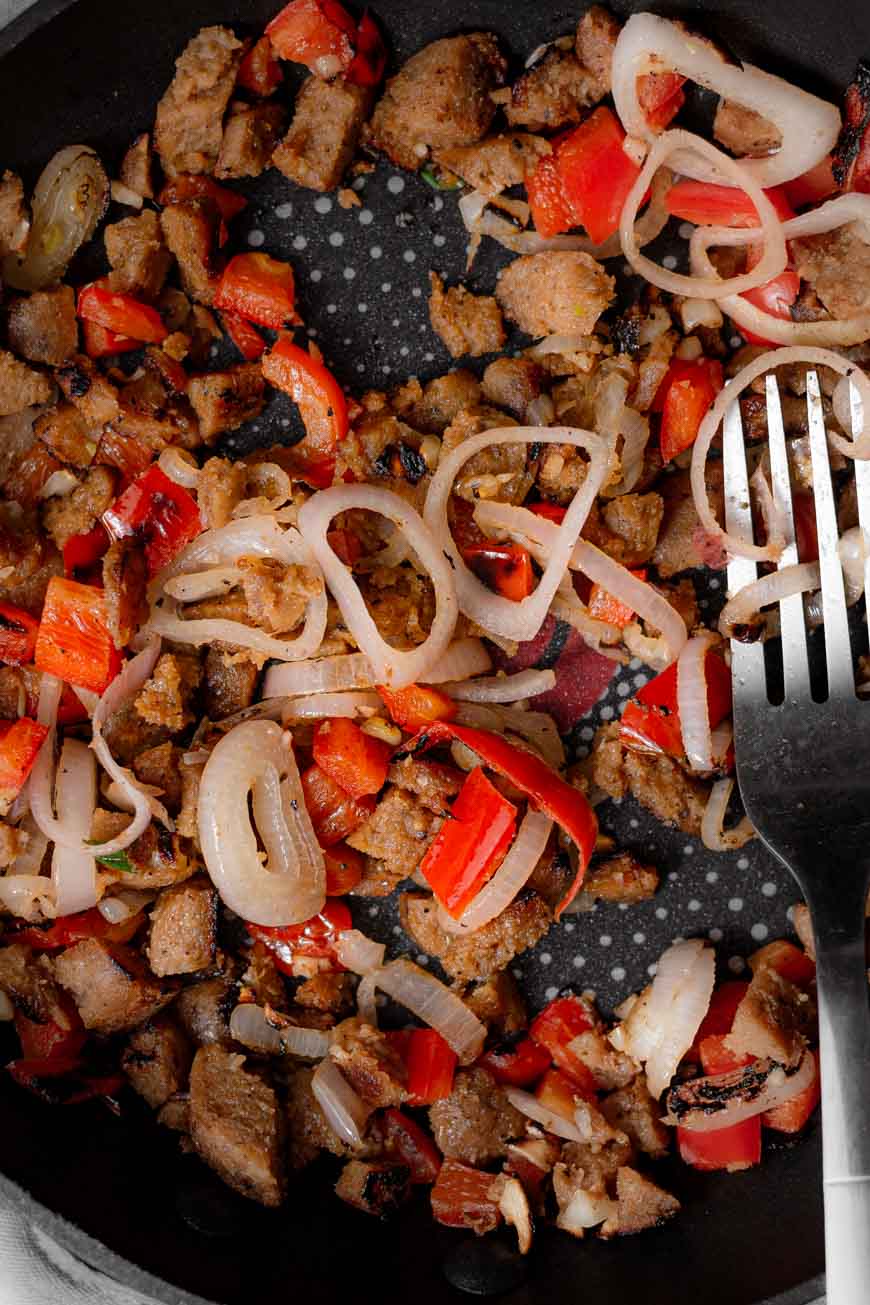 onions, vegan sausage and bell pepper in a pan.