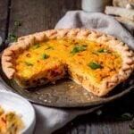 Whole vegan Just Egg quiche in a pie dish with a slice removed, showing creamy eggy filling and topped with green onions.