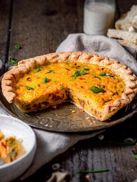 Whole vegan Just Egg quiche in a pie dish with a slice removed, showing creamy eggy filling and topped with green onions.